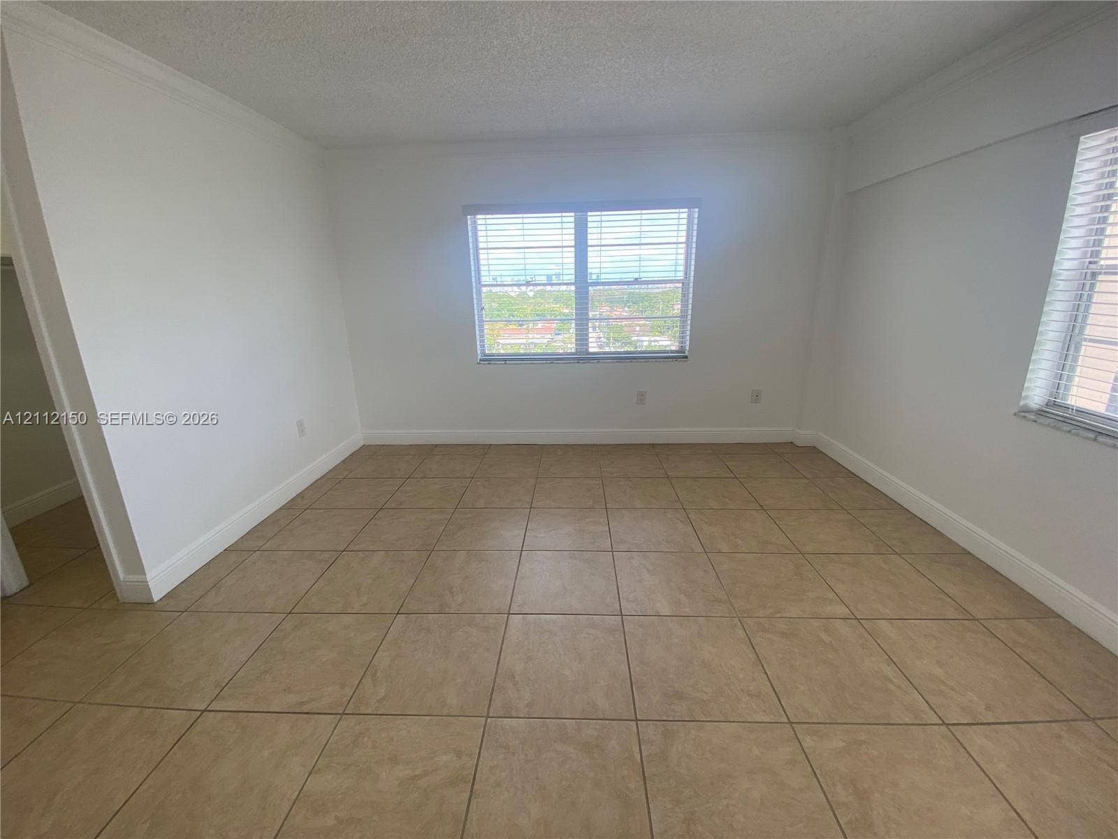 Neutral interior space featuring large-format tile flooring, textured ceilings, dual windows with horizontal blinds, and a built-in walk-in closet