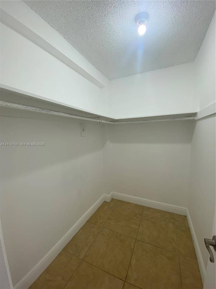 Walk-in storage space featuring ceramic tile flooring, built-in shelving, and a mounted hanging rod