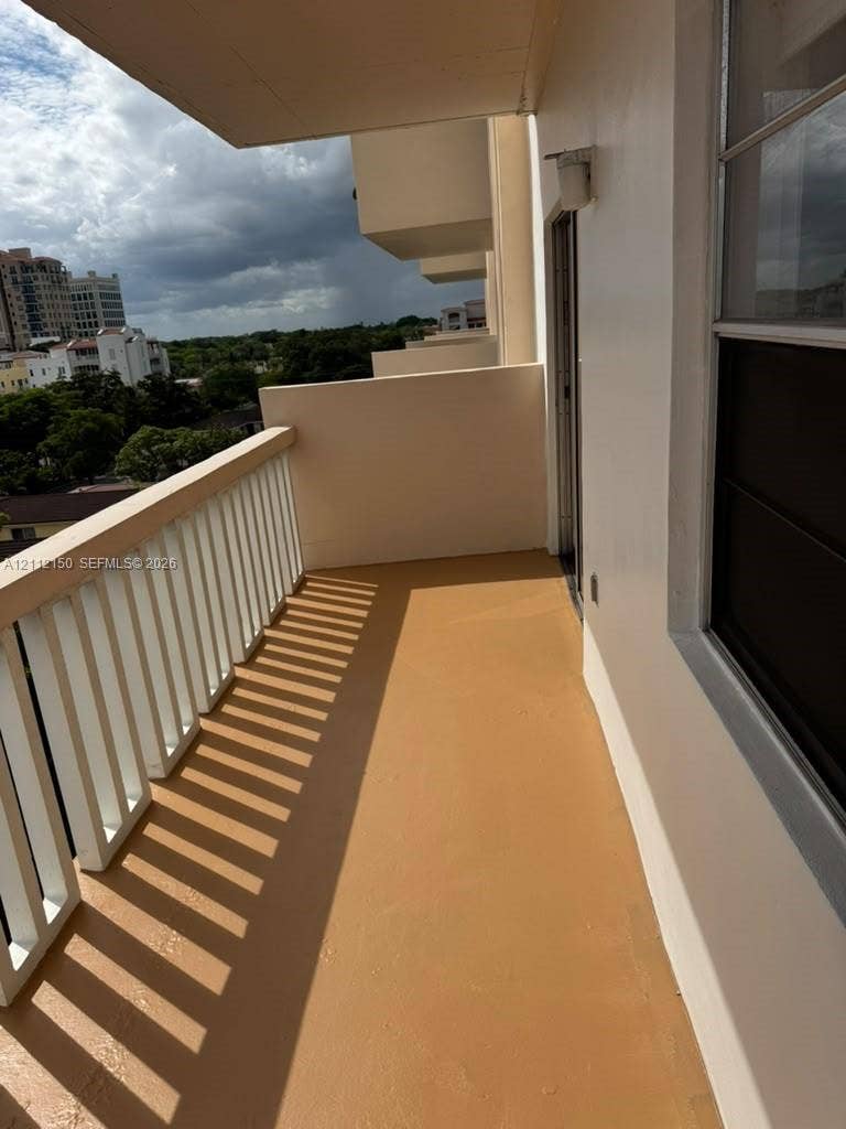Private balcony featuring a painted concrete floor, vertical spindle railing, and a wall-mounted exterior light fixture
