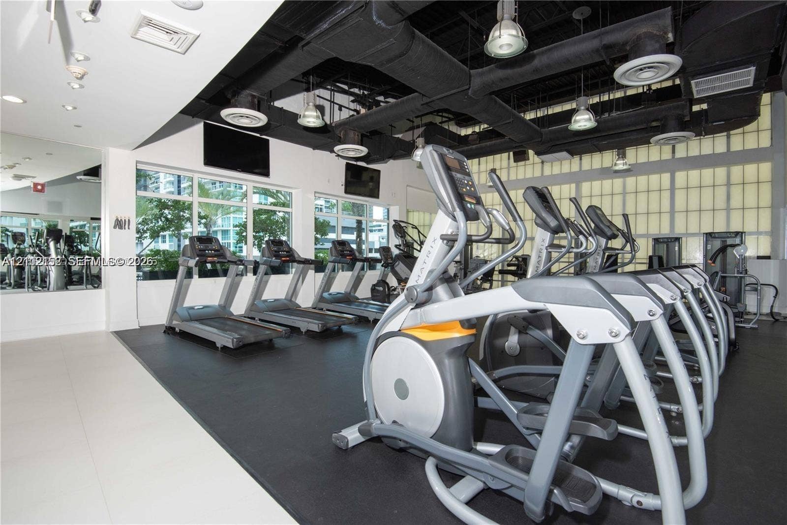Fitness center featuring large-format windows, industrial-style exposed ceiling, recessed lighting, rubber flooring, and full-wall mirrors