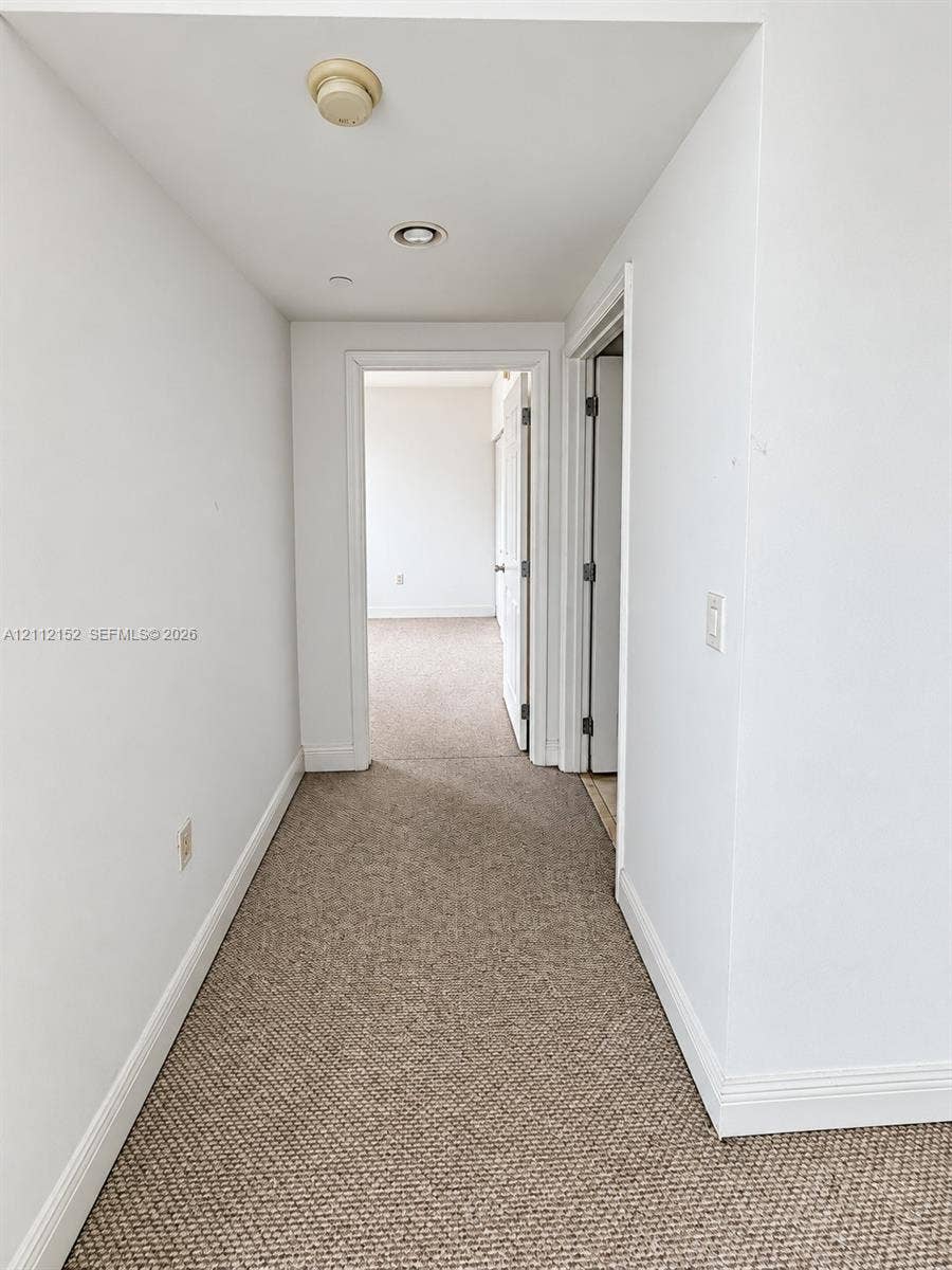 Hallway featuring neutral wall-to-wall carpeting, crisp white interior doors, and recessed ceiling lighting