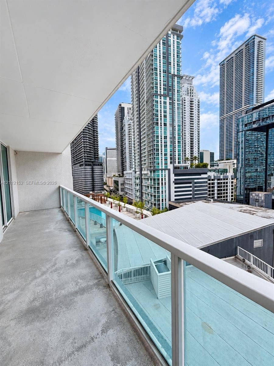 Covered balcony featuring concrete flooring and a glass-paneled railing