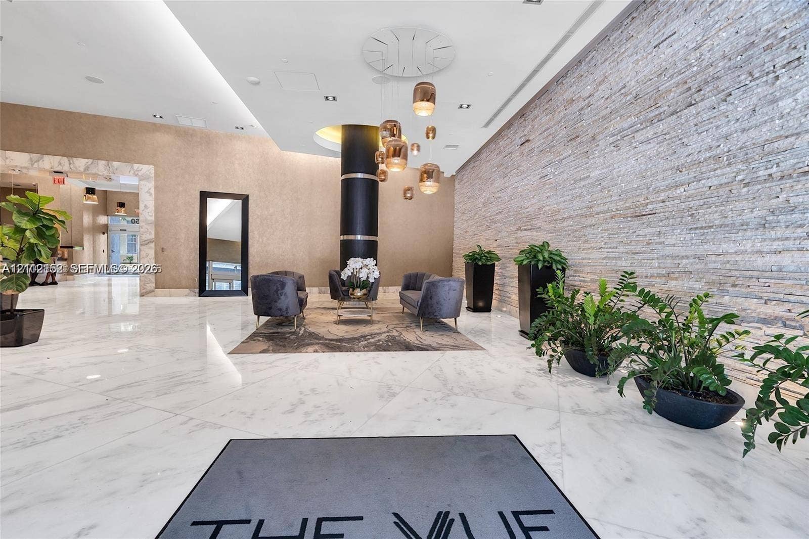 Grand lobby featuring polished stone flooring, a floor-to-ceiling textured stone accent wall, recessed lighting, and suspended metallic pendant fixtures