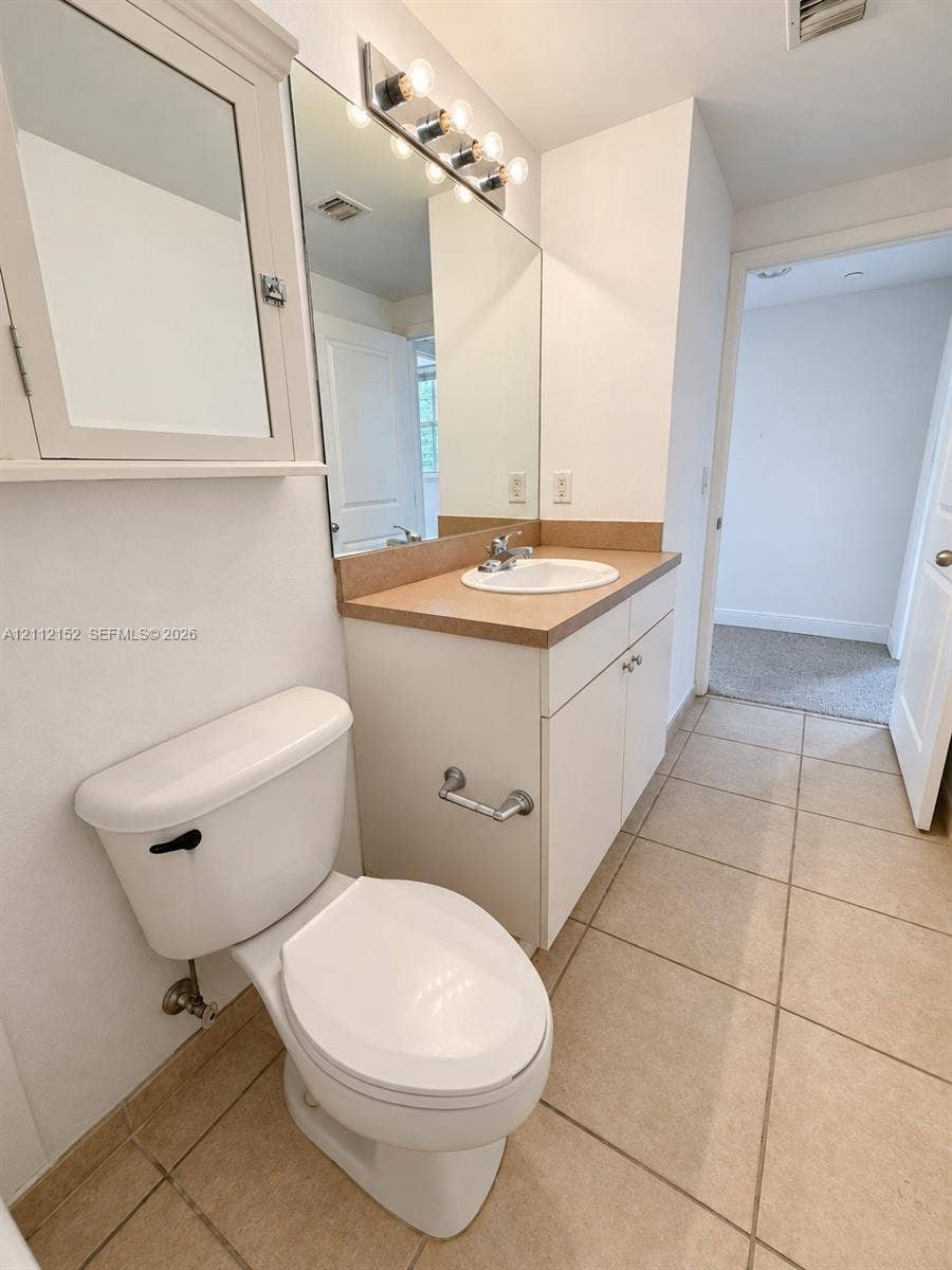 Bathroom featuring ceramic tile flooring, a white vanity cabinet with a solid-surface countertop, an oval drop-in sink, and a wall-mounted medicine cabinet