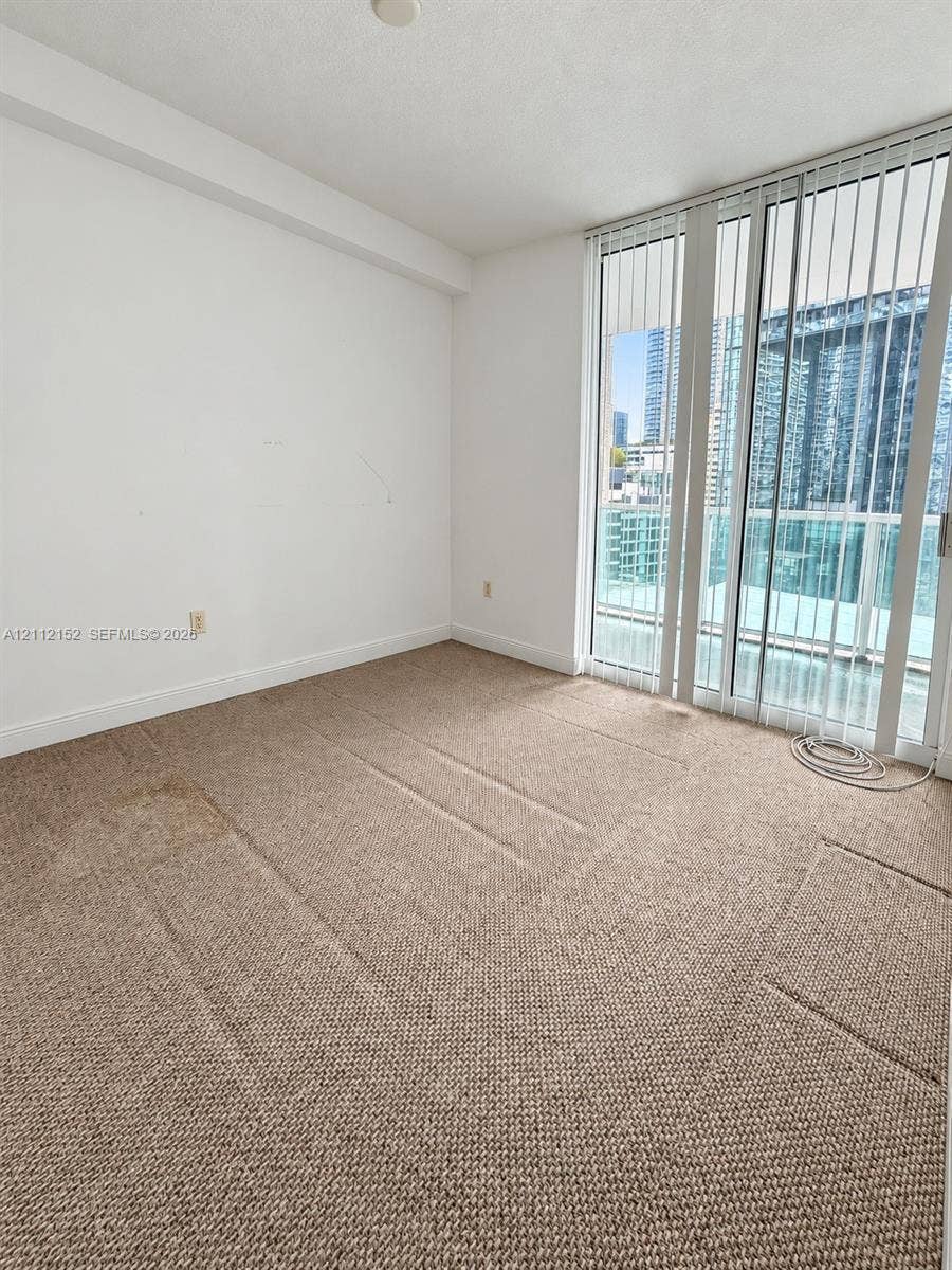 Wall-to-wall carpeting, full-height glass sliding door, and floor-to-ceiling windows with urban outlook