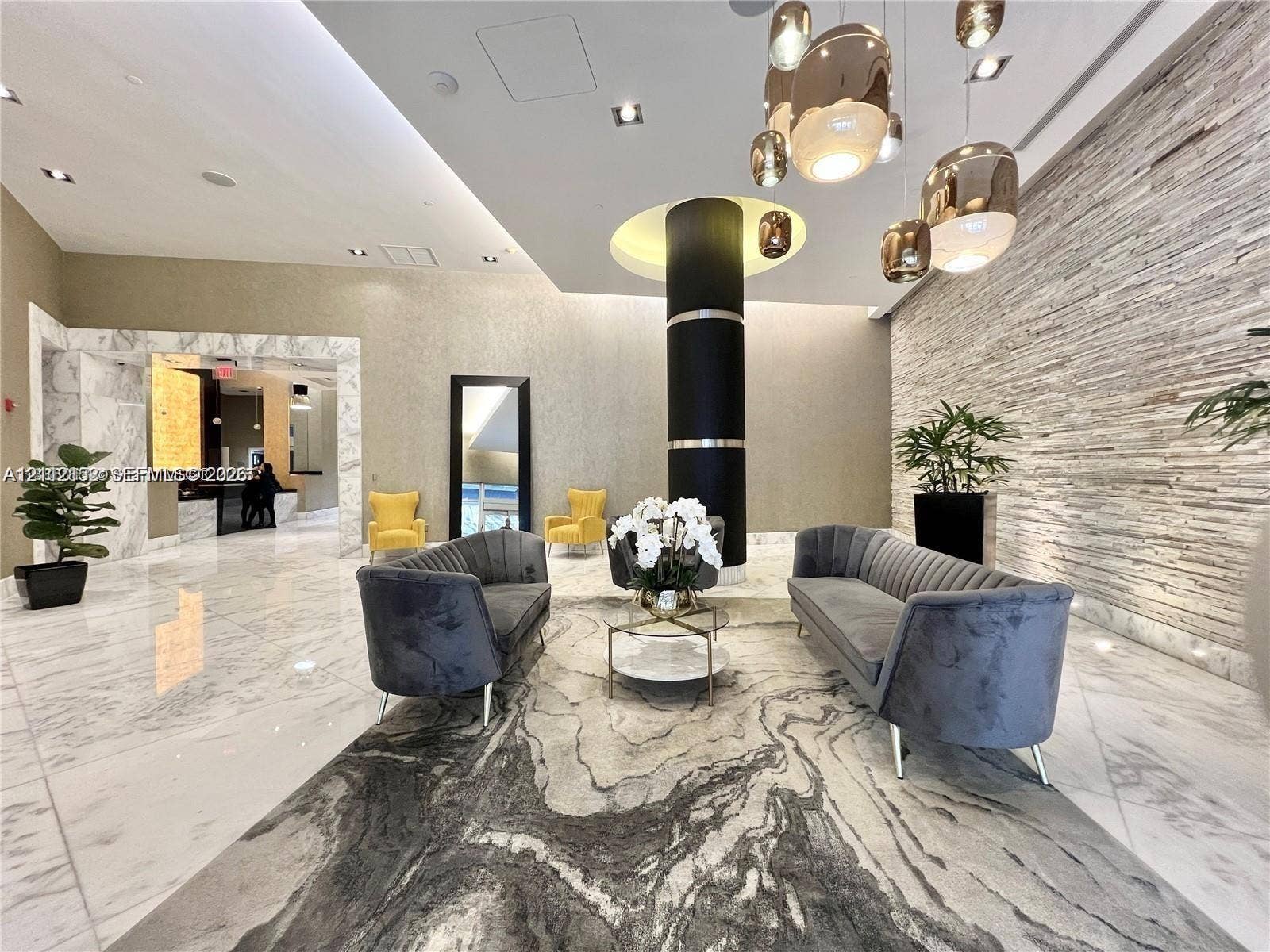 Lobby featuring polished stone flooring, a stacked stone accent wall, decorative metallic pendant lighting, a central structural column, and recessed ceiling lighting