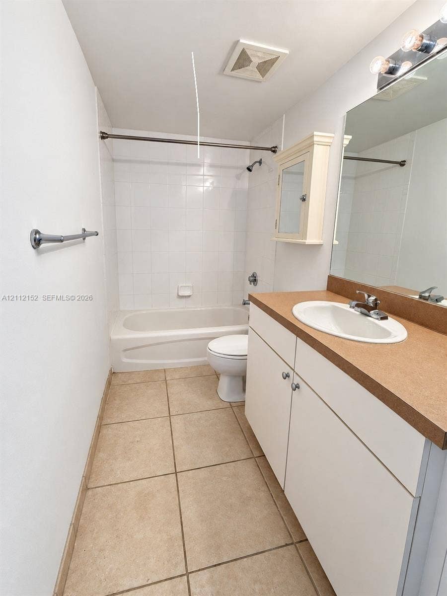 Bathroom featuring a white vanity cabinet with a solid surface countertop, an oval undermount sink, tiled flooring, and a shower-tub combination with white wall tile