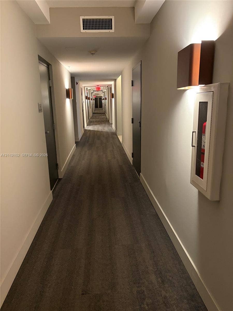 Hallway featuring wood-finish flooring, neutral wall tones, and architectural wall-mounted sconces