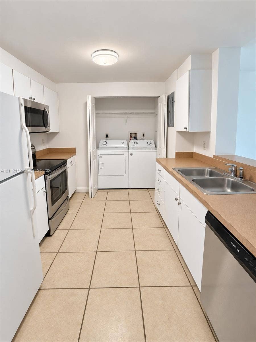 Kitchen featuring white cabinetry, solid surface countertops, stainless steel appliances, ceramic tile flooring, and an enclosed laundry closet
