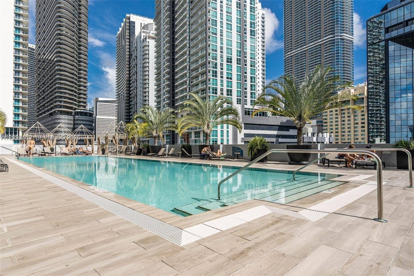 Swimming pool featuring wood-finish tile decking, metal handrails, integrated stair entry, and large-scale decorative planters