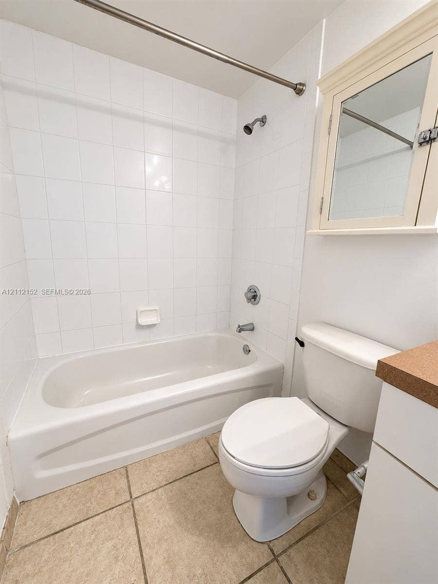 Bathroom featuring tile flooring, a tub-shower combination with full-height wall tiling, built-in medicine cabinet, and a solid-surface vanity countertop