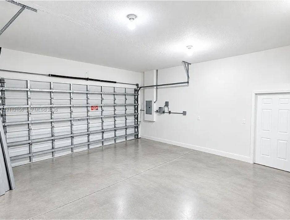 Finished garage interior featuring a smooth-finish concrete floor, high-ceiling structure, white-painted walls, and a multi-panel steel garage door