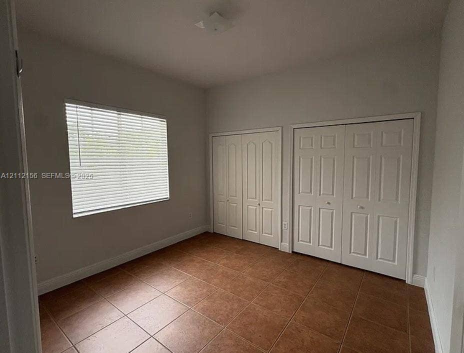 Room featuring neutral wall paint, tile flooring, two white panel-door closets, and a window with horizontal blinds