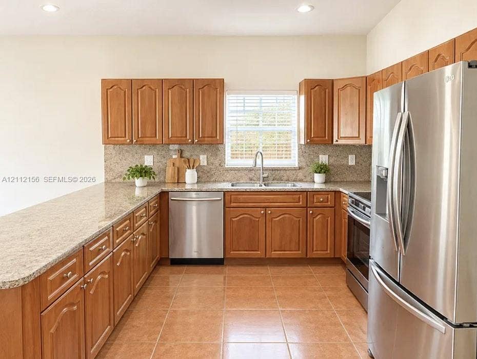 Kitchen featuring wooden cabinetry, stone-surface countertops, tile flooring, stainless steel appliances, and a double-basin sink