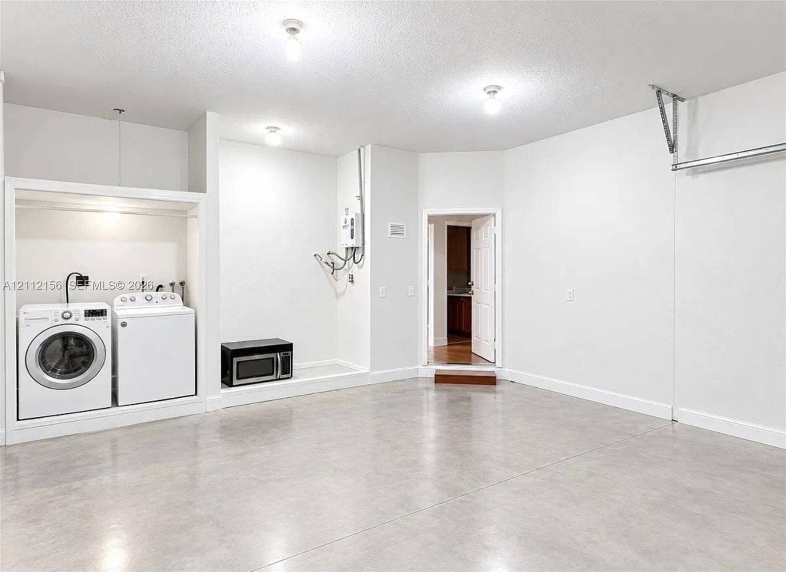 Finished interior space featuring smooth concrete flooring, white walls, and built-in laundry hookups with an overhead light fixture and wall-mounted tankless water heater