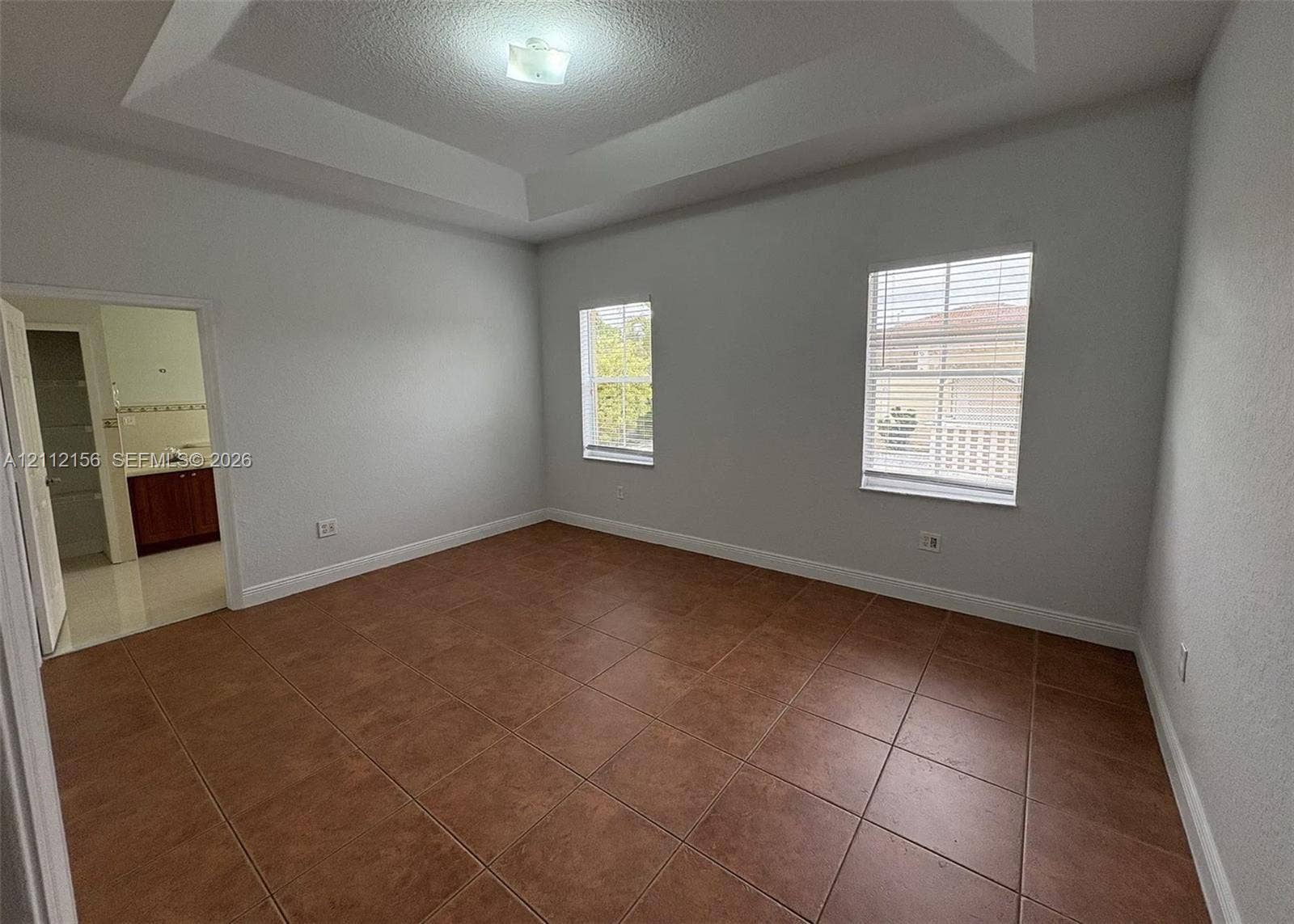 Room featuring a tray ceiling, square tile flooring, and dual windows with horizontal blinds