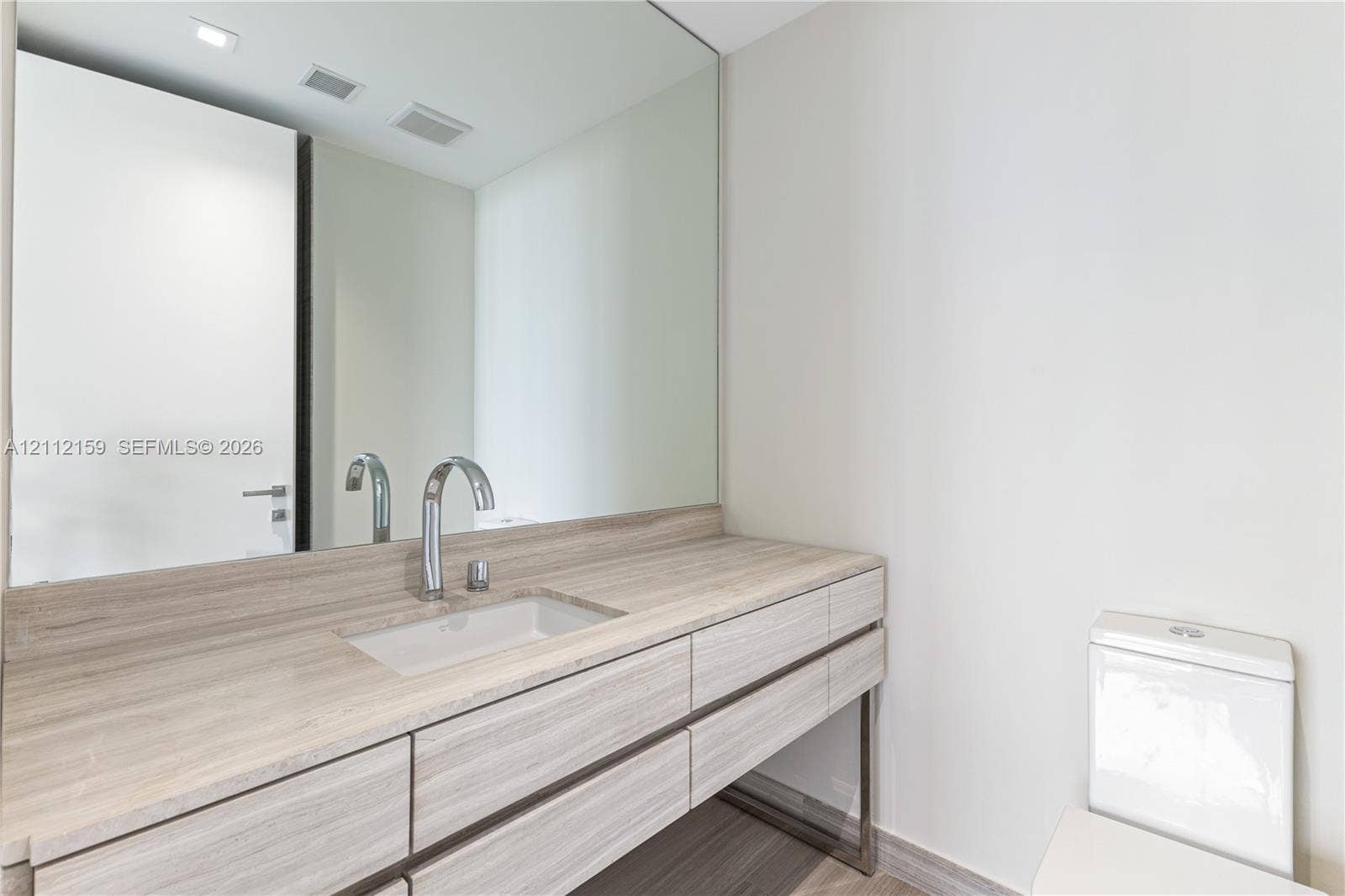 18975 Collins Avenue, #802, Sunny Isles Beach, Sunny Isles Beach, FL 33160 Floating vanity featuring wood-finish cabinetry, stone countertop with an integrated rectangular sink, wall-mounted polished chrome faucet, and a large seamless mirror
