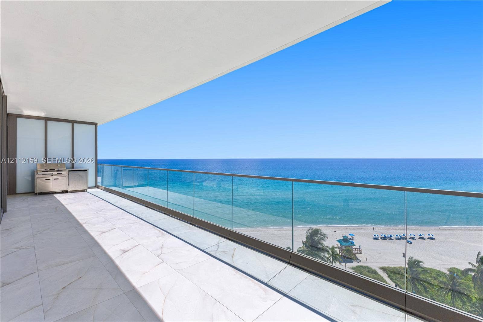 18975 Collins Avenue, #802, Sunny Isles Beach, Sunny Isles Beach, FL 33160 Spacious covered balcony featuring large-format stone tile flooring, a glass railing, and a built-in stainless steel outdoor kitchen station