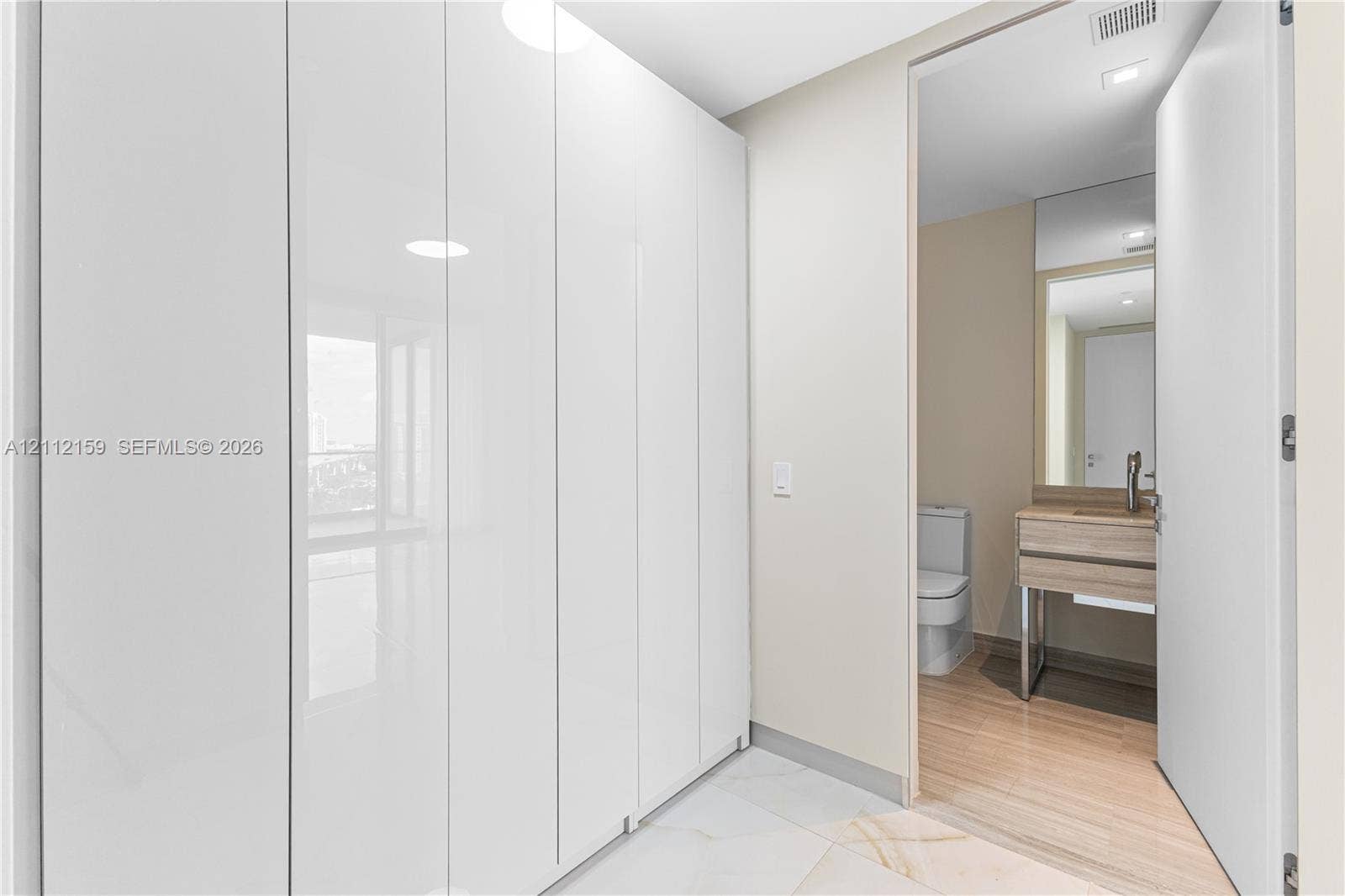 18975 Collins Avenue, #802, Sunny Isles Beach, Sunny Isles Beach, FL 33160 Floor-to-ceiling high-gloss white built-in cabinetry, large-format tile flooring, vanity with wood-finish cabinetry, rectangular vessel sink, and wall-mounted faucet