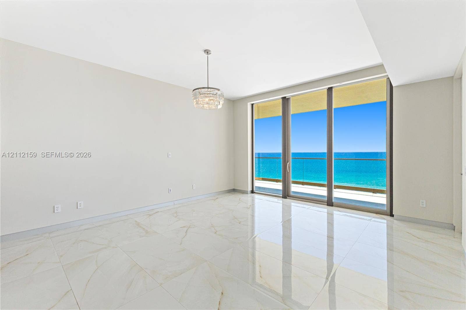 18975 Collins Avenue, #802, Sunny Isles Beach, Sunny Isles Beach, FL 33160 Polished stone flooring, crystal-accented chandelier, floor-to-ceiling glass sliding doors, and private balcony with ocean backdrop