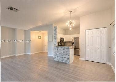 Interior featuring wood-finish flooring, stone-veneer accent half-wall, vaulted ceiling, multi-light chandelier, and floor-to-ceiling bi-fold closet doors