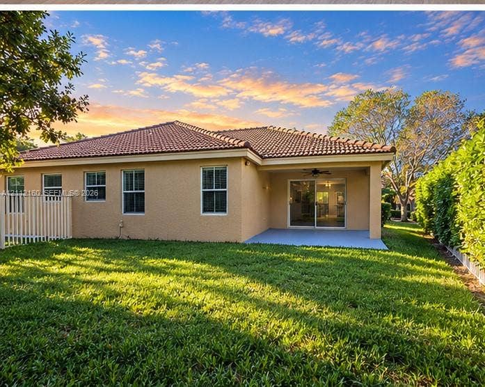 Exterior rear elevation featuring a tile roof, stucco siding, covered patio, and fenced backyard with mature trees