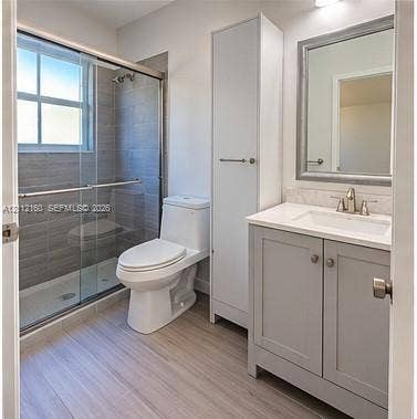 Bathroom featuring a vanity with a light-colored countertop, integrated tall cabinetry, a glass-enclosed shower with horizontal tile surround, and wood-finish flooring
