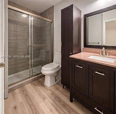 Bathroom featuring a dark wood-finish vanity with an integrated storage tower, wood-finish flooring, and a glass-enclosed shower with horizontal tile surround
