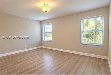 Neutral-toned walls, wood-finish flooring, two multi-pane windows with blinds, and an installed semi-flush mount light fixture