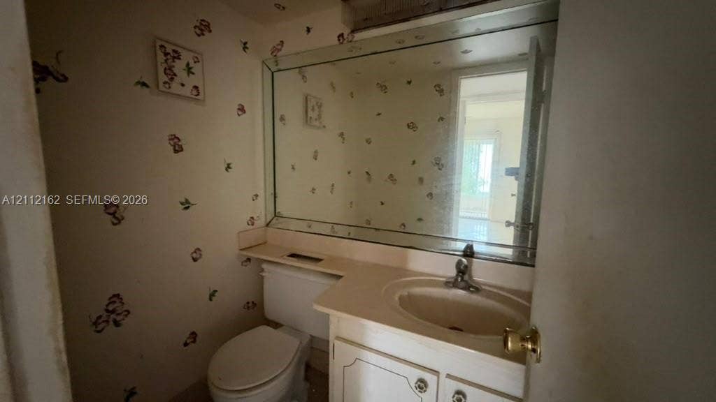 309 Fanshaw H, #309, Boca Raton, FL 33434 Vanity featuring a solid-surface countertop with an integrated basin, white cabinetry, a large wall-mounted mirror, and a porcelain toilet