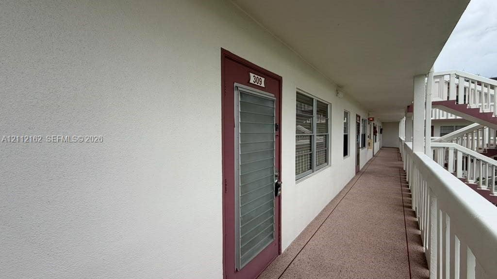 309 Fanshaw H, #309, Boca Raton, FL 33434 Exterior corridor featuring stucco wall finishes, metal louvered storm doors, multi-pane windows, and a covered balcony with a white railing system