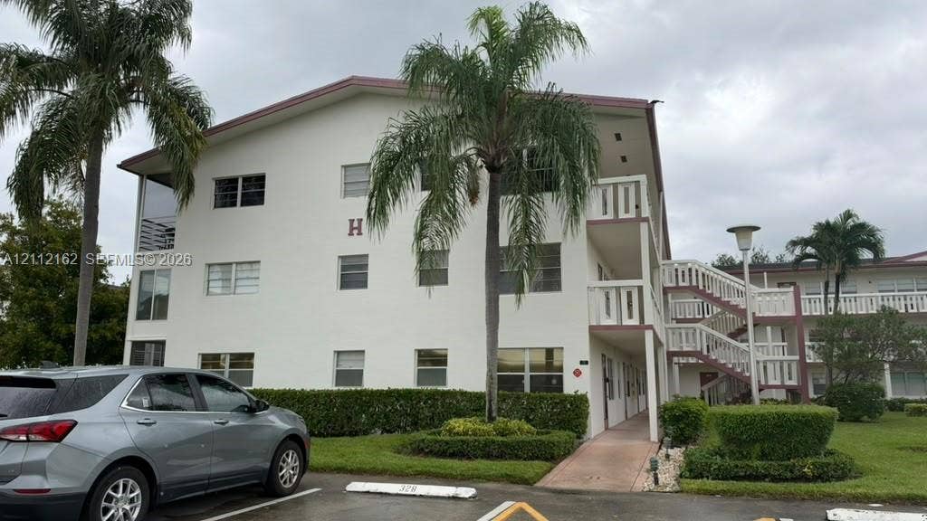 309 Fanshaw H, #309, Boca Raton, FL 33434 Three-story building exterior featuring smooth stucco siding, railed balcony access, open-air staircase, and integrated landscaping