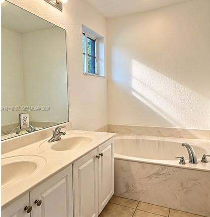 Double vanity featuring integrated solid-surface countertops, recessed sinks, large wall-mounted mirror, and a soaking tub with stone-patterned surround