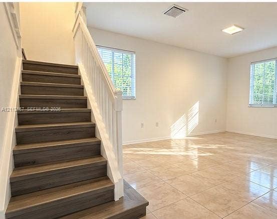Staircase with wood-finish treads and white balusters, ceramic tile flooring, and multi-pane windows with horizontal blinds