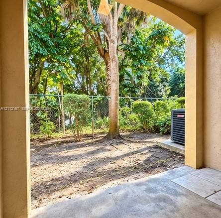 Covered patio featuring concrete flooring, an arched entryway, chain-link perimeter fencing, and mature landscape