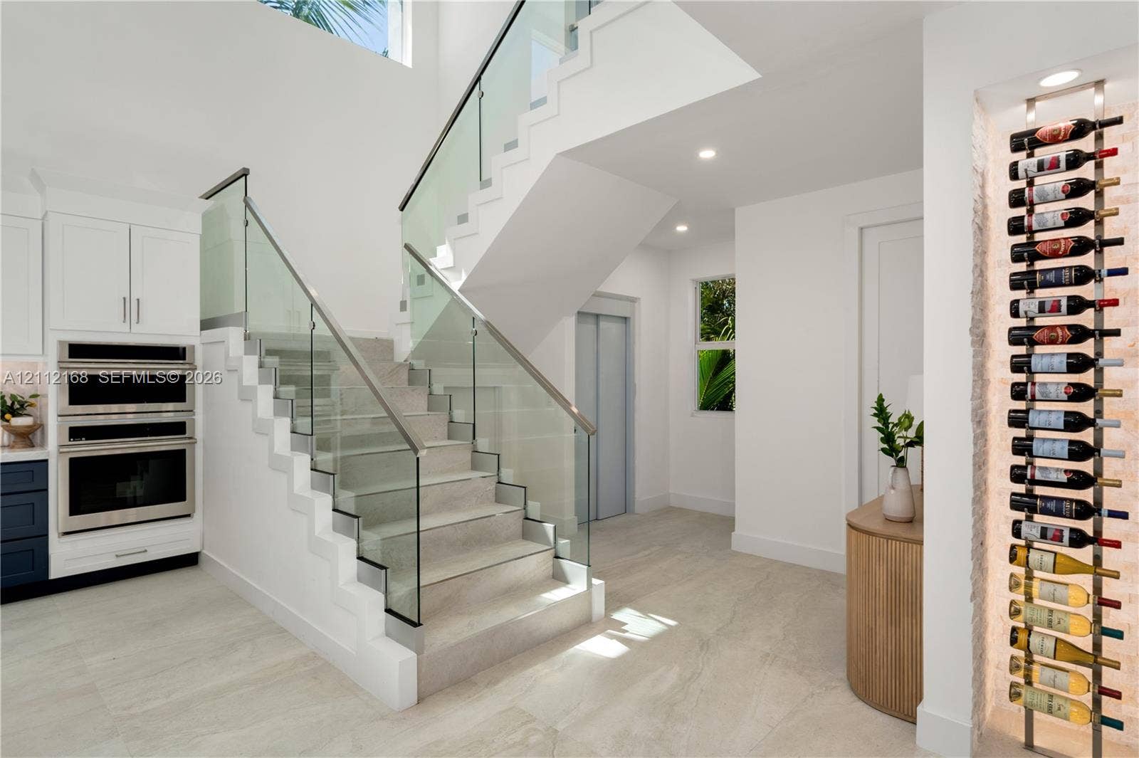 1041 E Buttonwood Drive, Sugarloaf Key, FL 33042 Open-riser staircase featuring a glass-panel railing, built-in stainless steel double wall ovens, recessed wine storage rack, and light-toned tile flooring