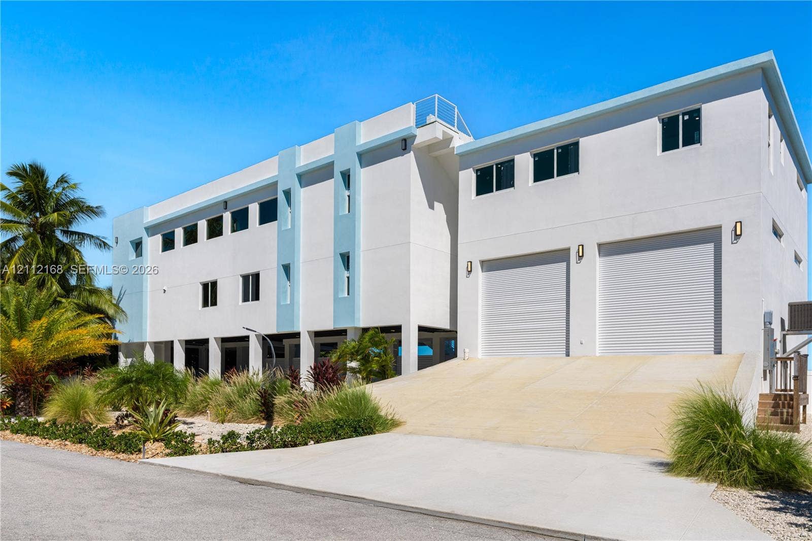 1041 E Buttonwood Drive, Sugarloaf Key, FL 33042 Multi-story contemporary exterior featuring a concrete facade, dual roll-up garage doors, a concrete vehicle ramp, and exterior wall-mounted lighting