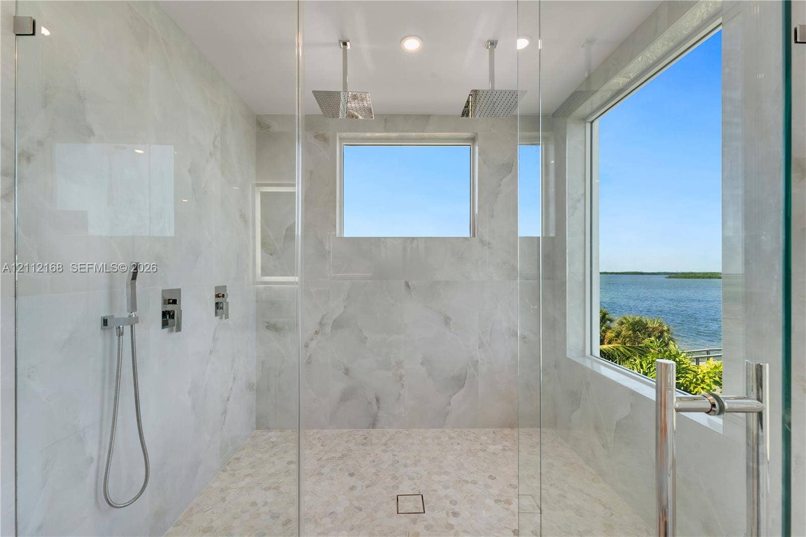 1041 E Buttonwood Drive, Sugarloaf Key, FL 33042 Walk-in shower featuring floor-to-ceiling stone-patterned tile, dual ceiling-mounted rainfall showerheads, a handheld sprayer, a glass enclosure, and a large window