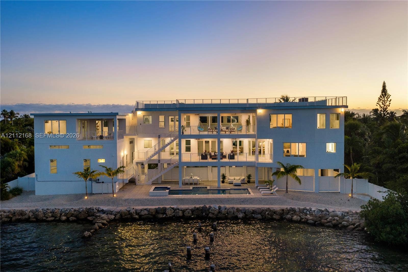 1041 E Buttonwood Drive, Sugarloaf Key, FL 33042 Waterfront multi-story residence featuring a private swimming pool, expansive stacked balconies with metal railings, a rooftop terrace, and a stone-lined bulkhead