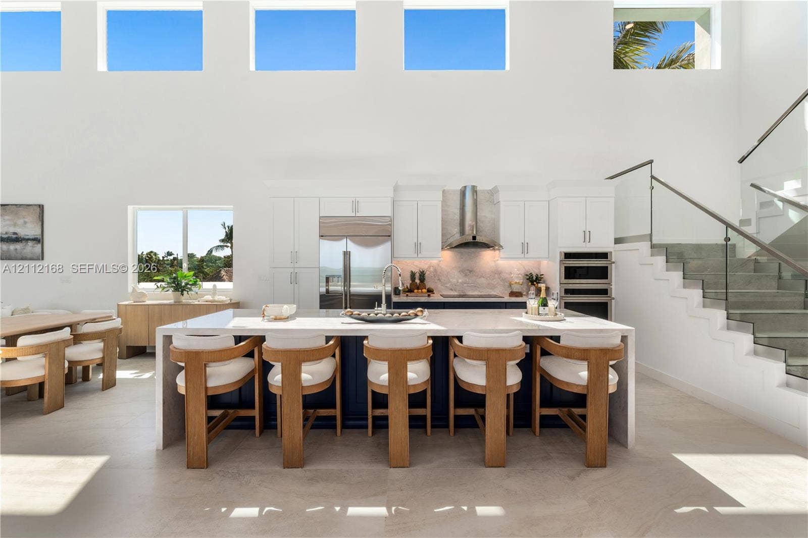 1041 E Buttonwood Drive, Sugarloaf Key, FL 33042 Double-height ceilings with transom windows, large center island with waterfall countertop, stainless steel kitchen appliances, and glass-paneled staircase railing