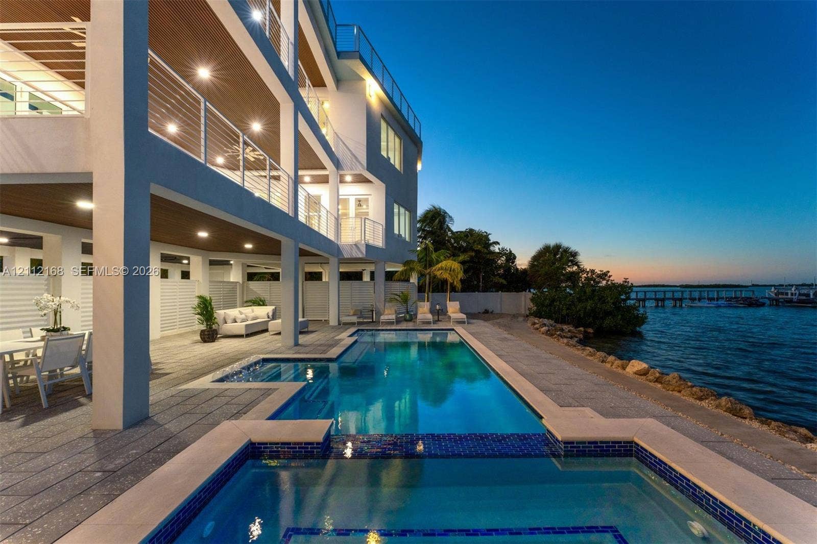 1041 E Buttonwood Drive, Sugarloaf Key, FL 33042 Waterfront multi-level residence featuring a custom swimming pool with integrated spa, expansive covered lanais, metal cable railings, and textured stone-finish decking