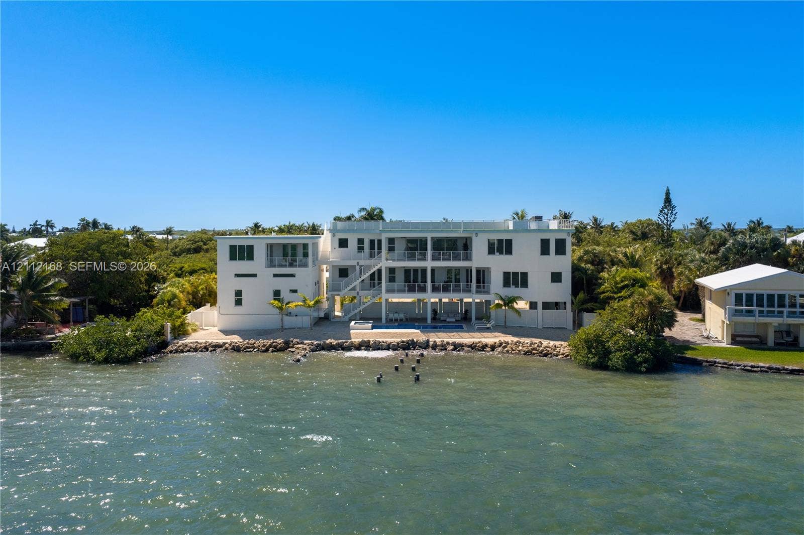 1041 E Buttonwood Drive, Sugarloaf Key, FL 33042 Waterfront multi-story residence featuring tiered exterior balconies, a ground-level swimming pool, and stone-reinforced shoreline