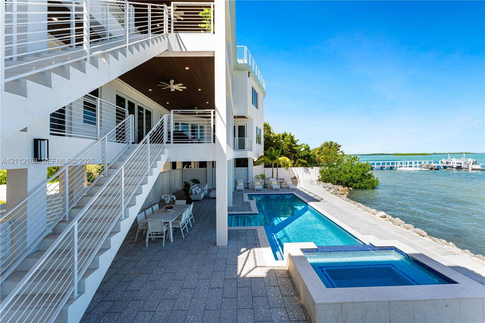 1041 E Buttonwood Drive, Sugarloaf Key, FL 33042 Multi-level exterior featuring a private swimming pool with integrated spa, paved pool deck, metal stair railings, and direct water access with a private dock