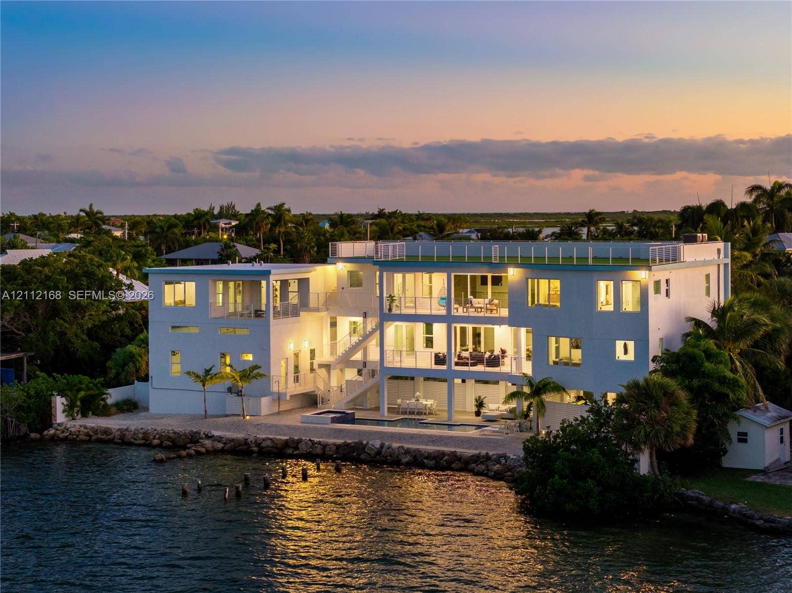 1041 E Buttonwood Drive, Sugarloaf Key, FL 33042 Waterfront residence featuring multi-level covered balconies, a rooftop deck with railing, a built-in pool, and a stone-lined bulkhead