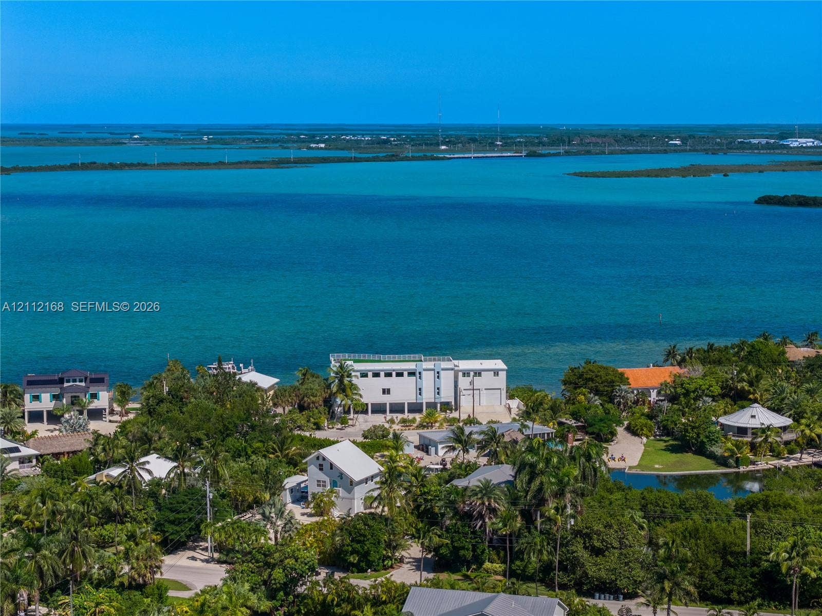 1041 E Buttonwood Drive, Sugarloaf Key, FL 33042 Waterfront property featuring direct coastal access, multi-level structural design, white exterior cladding, and expansive surrounding tropical vegetation