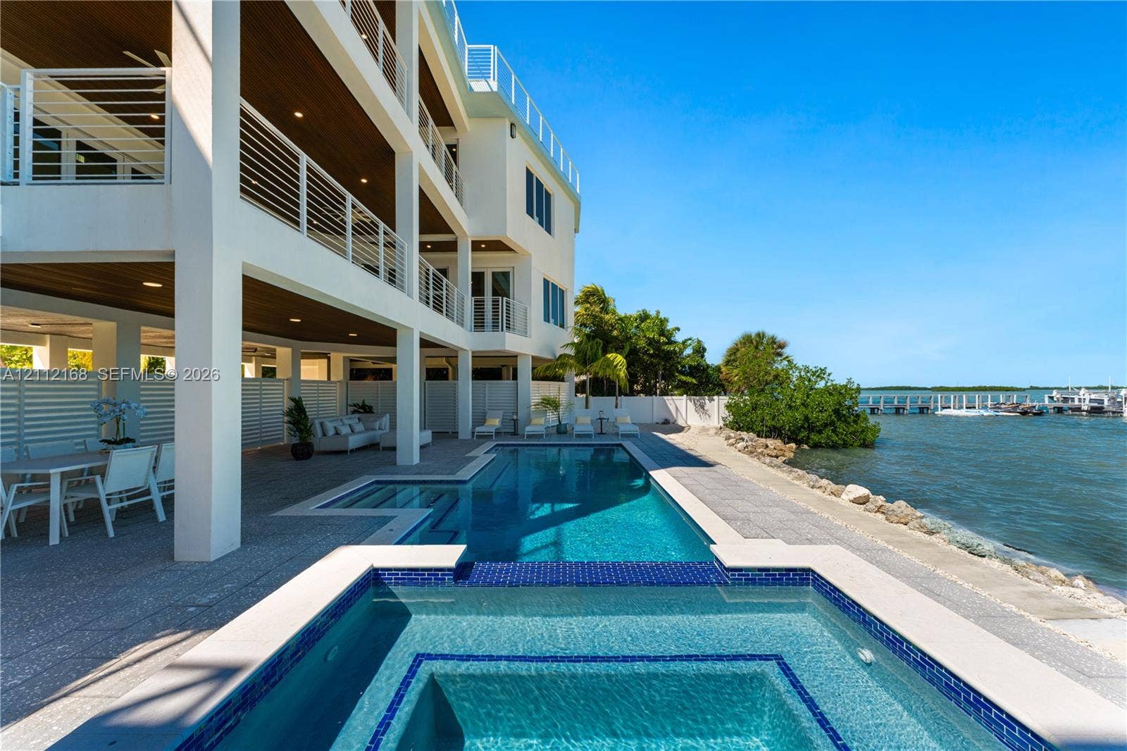 1041 E Buttonwood Drive, Sugarloaf Key, FL 33042 Multi-level exterior featuring tiered balconies with metal railings, a covered patio with recessed lighting, an integrated swimming pool and spa, and bulkhead waterfront access