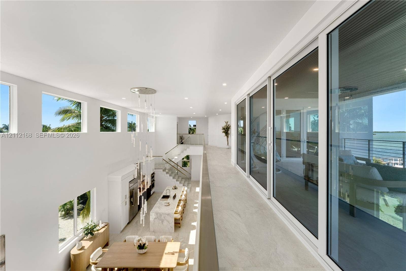 1041 E Buttonwood Drive, Sugarloaf Key, FL 33042 Open-concept upper level featuring large-format tile flooring, a multi-story glass pendant chandelier, expansive floor-to-ceiling sliding glass doors, and a metal-railing staircase