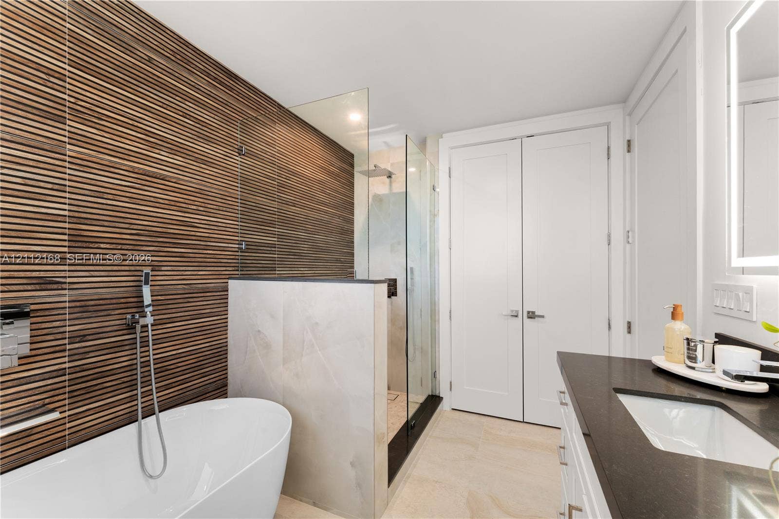 1041 E Buttonwood Drive, Sugarloaf Key, FL 33042 Bathroom featuring a textured wood-slat feature wall, freestanding soaking tub, walk-in glass-enclosed shower, dark countertop with an integrated basin, and double-door storage