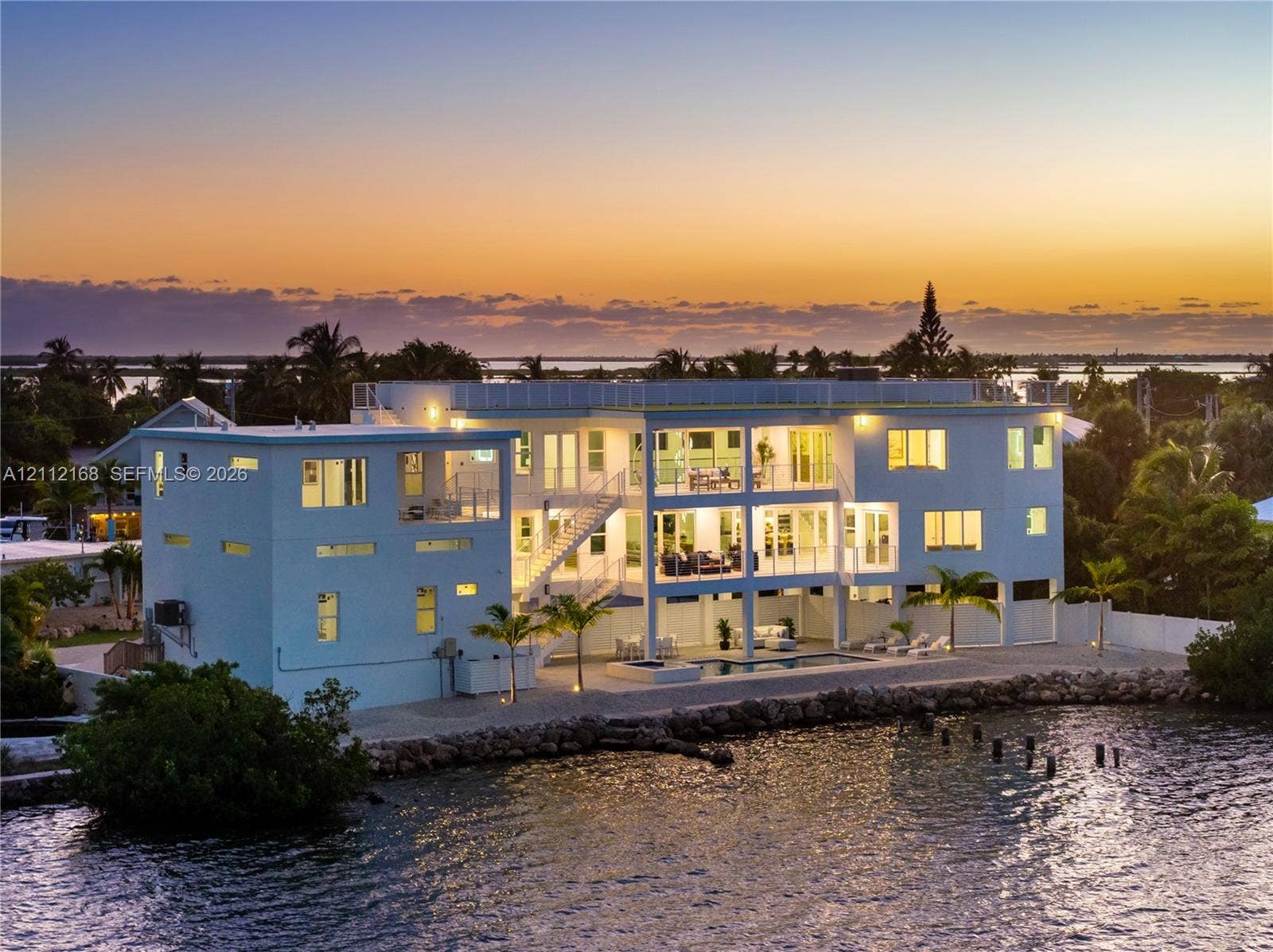 1041 E Buttonwood Drive, Sugarloaf Key, FL 33042 Waterfront multi-story residence featuring tiered balconies, a rooftop deck, exterior staircase, and a ground-level swimming pool