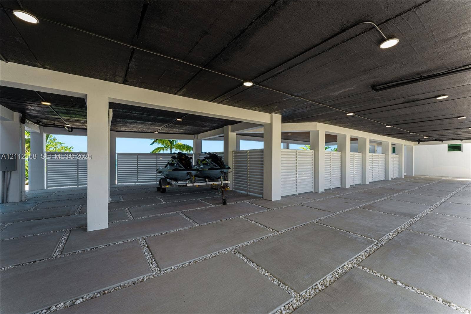 1041 E Buttonwood Drive, Sugarloaf Key, FL 33042 Covered parking area featuring large-format concrete pavers with stone aggregate borders, structural support pillars, white privacy screening, and recessed lighting